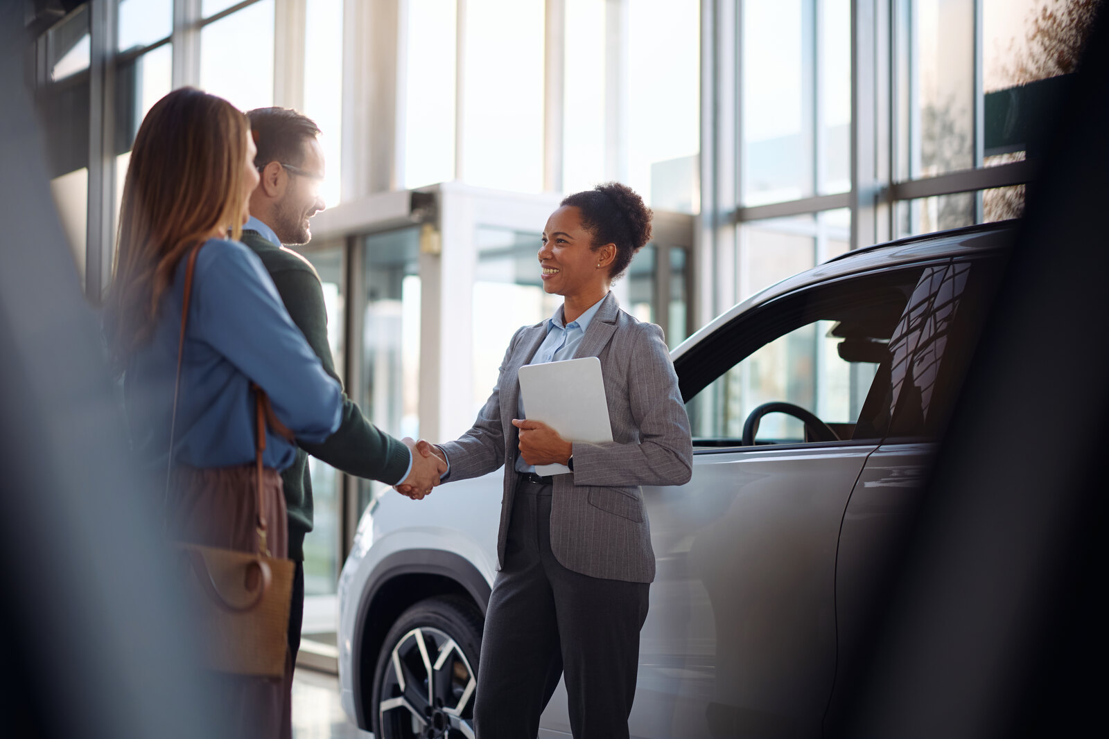 An F&I consultant closing a deal with customers beside a car at a dealership